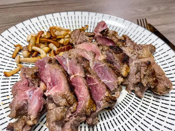roast beef with mushrooms on a white plate on a wooden table