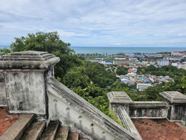 Eski bir taş merdiven manzarası kıyı kasabasına bakar yemyeşil, renkli binalar ve mavi okyanus ufuk çizgisini bulut gibi bulutlu bir gökyüzünün altında karşılar..