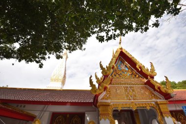 Parlak bir gökyüzü ve yemyeşil tarafından çerçevelenmiş, karmaşık altın detaylarıyla süslenmiş çarpıcı bir tapınak..