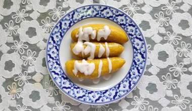 Bu resim, dekoratif bir tabakta zarif bir şekilde sunulan kremalı sosla serpiştirilmiş tatlı muzları içeriyor. Yemek severler ve aşçılar için ideal..