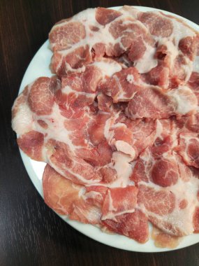 Beyaz bir tabakta taze dilimlenmiş domuz eti, çeşitli yemekler pişirmek için ideal. Kaliteli malzemeler arayan aşçılar için mükemmel..