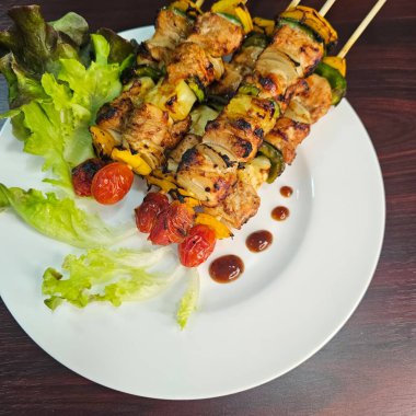 Beyaz tabakta servis edilen ızgara sebze ve et şişleri için iştah açıcı bir düzenleme. Parlak renkler ve taze malzemeler her yemek için mükemmel bir ağız sulandırıcı görüntü yaratır..