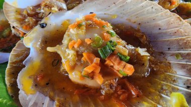 Üzerinde taze sebzeler bulunan deniz tarakları bulunan ve kabuklarında güzelce sunulan cazip bir deniz ürünleri tabağında şevkat gösterin. Aşçılık meraklıları için ideal..