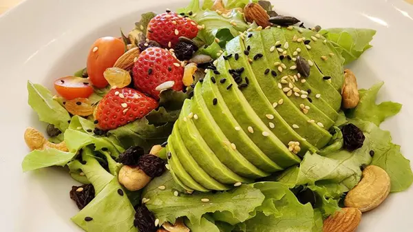 Dilimlenmiş avokado, çilek, vişneli domates ve fındık içeren lezzetli ve besleyici bir yemek için tohumla kaplı canlı bir salatanın tadını çıkarın. Sağlıklı yemek için mükemmel.!