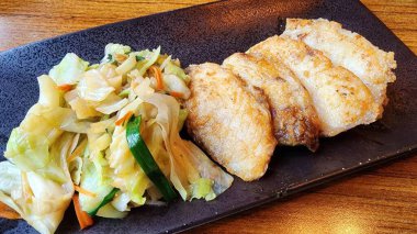 Bir tabak kızarmış balık filetosu. Yanında canlı sebze kızartması ve lahana ve taze malzemelerle servis ediliyor. Sağlıklı bir yemek için mükemmel..