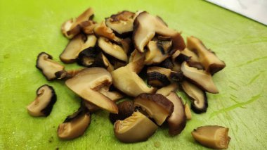 Canlı yeşil bir kesme tahtasına yerleştirilmiş taze dilimlenmiş Şiitake mantarları. Bu resim, sağlıklı ve organik bileşenleri vurgulamak için mutfak projeleri için mükemmel..