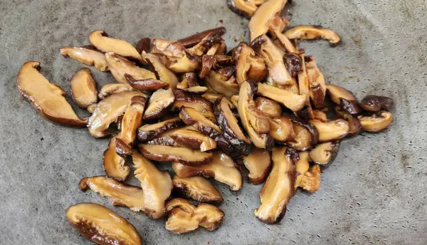 Gri bir yüzeye yerleştirilmiş dilimlenmiş shiitake mantarları koleksiyonu. Çeşitli yemekleri geliştirmek için mükemmel. Mutfak meraklıları ve sağlıklı yemek tarifleri için ideal..