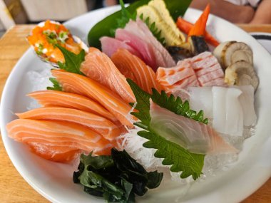 Somon, ton balığı ve karides içeren taze deniz mahsulleri içeren canlı bir sashimi tabağı. Lezzetli bir mutfak deneyimi için buzla süslenmiş..