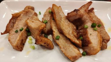 Beyaz bir tabakta servis edilen ızgara domuz eti, yeşil soğanla süslenmiş, et severler ve aşçılar için nefis ve lezzetli bir yemek sergileniyor..