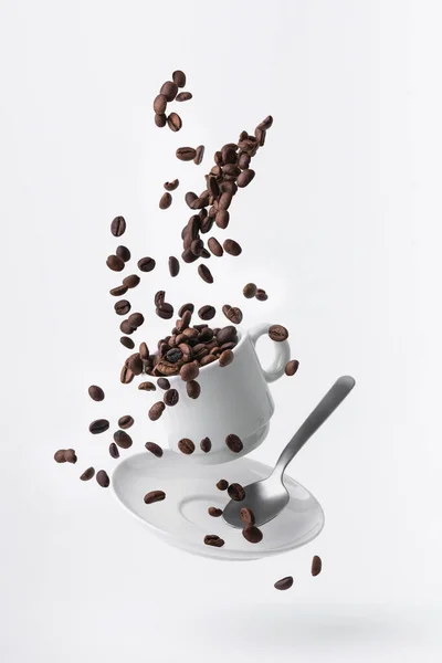 stock image roasted coffee beans spilled from a floating cup and a teaspoon isolated on white background