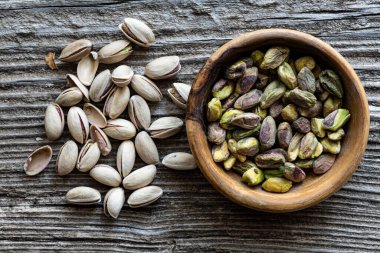 Top view, on an old wooden background, extreme closeup, a pile of pistachios and a bowl with shelled pistachios