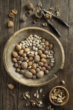Seen from above, on an old wooden background, a nutcracker, a bowl with shelled walnuts and a vintage wooden plate contains mixed nuts