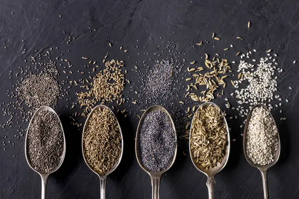 Top View Some Spoons Variety Organic Seeds Black Textured Background — Stock Photo, Image