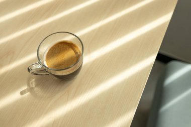 Bir fincan kahvenin yakın çekimi ahşap masanın üzerinde, pencereye doğru gölgeli çizgili bir şekilde masaya ve zeytin kanepeye konur. Düz yatıyordu. Üst görünüm.