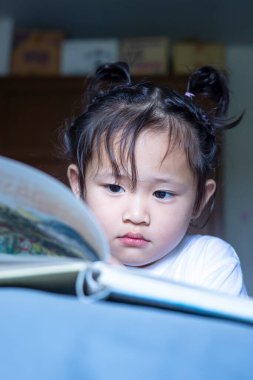 Geceleri yatakta masal okuyan Asyalı tatlı küçük bir kız..