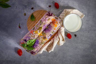 Top view of a loaf of bread with edible flowers, flamboyant, west indian jasmine, roses, and cereal grains, homemade bread, healthy eating. Close-up. Flat lay.