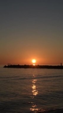 Sahildeki kayalıklarda gün batımında insanlar yürüyor. 4K Dikey