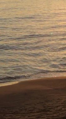 Gün batımında sahile sakin dalgalar geliyor. 4K Dikey