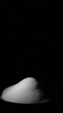 Siyah tabakta dönen beyaz şeker. 4K Dikey