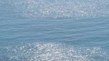 Güneşli bir günde beyaz kıvılcımlar saçan ılık mavi bir deniz.