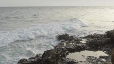 Dalgalar gün batımında kayalara çarpıyor.