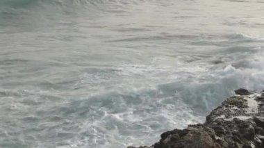 Dalgalar gün batımında kayalara çarpıyor.