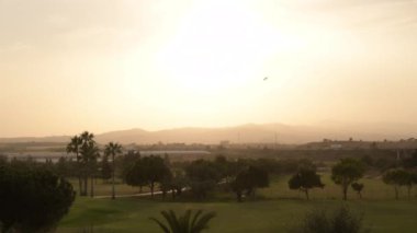 Golf sahasından gün batımında, arka planda dağlar ve otoyol var.