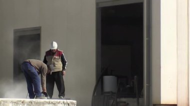 Tuğlacı endüstriyel bir depoda büyük bir tuğlayı öğütücüyle kesiyor.