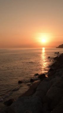 Kayalık sakin bir plajda gün batımı. 4K Dikey