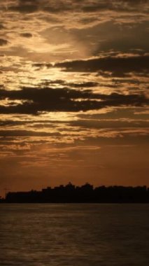 Kıyı şehrinde gün batımında bulutlar ve güneş. Zaman Süreleri