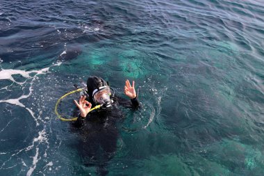 May 24, 2017 - Tuscany, Italy: A woman wear a full face diving mask on the surface of the sea level giving the OK