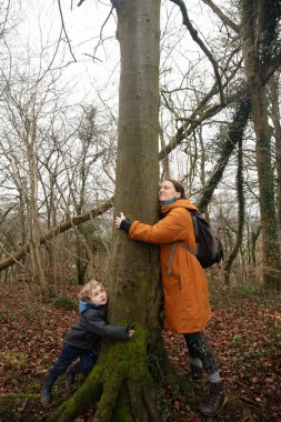 Anne ve oğul, mutlu bir şekilde bir ağaca sarılıp doğayla bağ kurmaya çalışıyorlar..