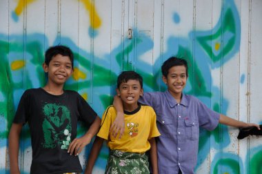 Pamekasan, Jawa Timur, Madura island, Indonesia - June 4, 2010: group of Indonesian children looking at camera with a smile In front of a garage with graffiti clipart