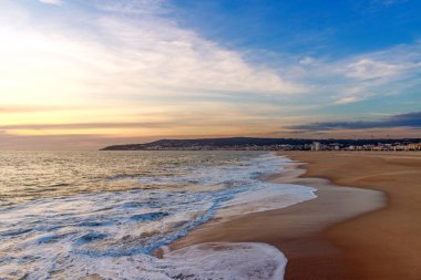 Deniz kıyısının renkli akşam manzarası, şehrin yakınındaki geniş kumlu sahil ve bulutlu akşam gökyüzü, Figueira da Foz, Portekiz