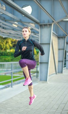 Kadın ısınıyor ve yol boyunca koşuyor, dışarıda spor yapıyor.