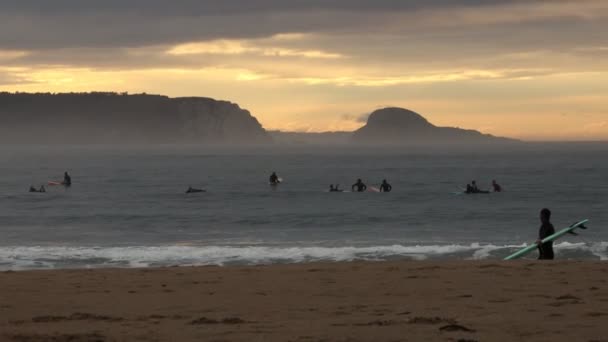 霧の風 美しい崖 日没の背景に対して夜間に海でサーフィンを練習する人もいます — ストック動画