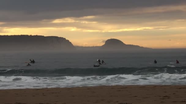霧の風 美しい崖 日没の背景に対して夜間に海でサーフィンを練習する人もいます — ストック動画