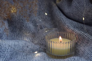 Çelenkle süslenmiş sıcak bir battaniyenin üzerinde yanan bir mum. Sıcak bir atmosfer ve mum.. 