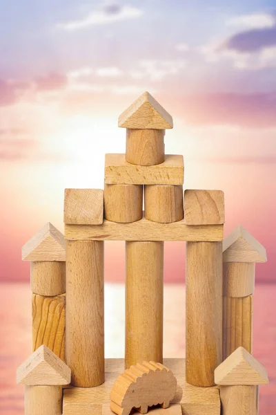 House made of wood. Wooden toy castle made of cubes, cylinders, triangles and a sheep at the entrance over abstract blurred sunset. Wooden toy blocks. Macro.