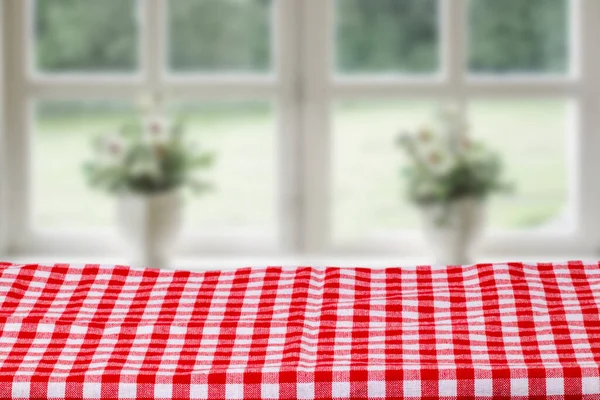 Empty table product. Closeup of a empty red tablecloth or napkin over abstract blurred bright windows background. Template for food and product display montage.