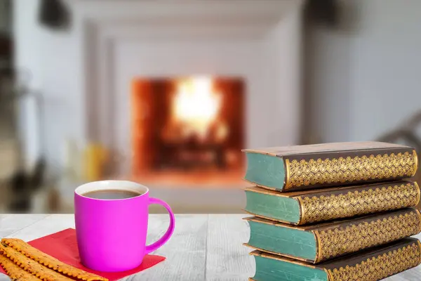 Winter christmas books background. A stack of antique books with a coffee mug and Italian pastries on a wooden table over abstract blurred fireplace. Reading books in holiday time.