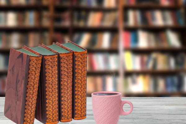 Books backgrounds. Closeup of antique books with a coffee mug on a wooden table over abstract blurred bookshelf in library. Education concept. Teacher day.