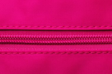 Fermuarlı arka plan dokusu. Kapalı plastik bir fermuarın, elastik pembe naylon kumaştan yapılmış bir sırt çantasına bağlanmış yüksek çözünürlüklü yakın plan fotoğrafı. Makro fotoğraf.