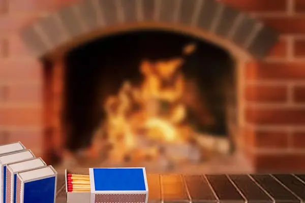 Matches, fire and smoke. Several matchboxes, including an open one, on a wall ledge in front of an abstract, blurred burning fireplace. Space for copying.