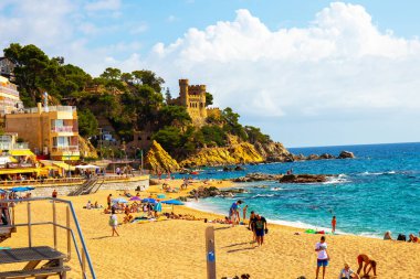 Lloret de Mar, Katalonya, İspanya, 02 Ekim 2019. 1940 'lardan kalma şatoya benzeyen Castell de Plaja' nın aşağısındaki Lloret de Mar plajındaki turistler. Costa Brava.