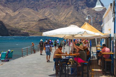 Puerto de las Nieves, island of Gran Canaria Spain  20 Jul 2024. Tourists and locals on the streets with typical white-blue romantic architecture port town. clipart