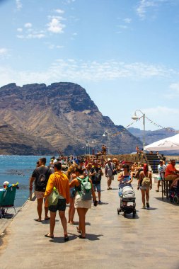 Puerto de las Nieves, island of Gran Canaria Spain  20 Jul 2024. Tourists and locals on the streets with typical white-blue romantic architecture port town. clipart