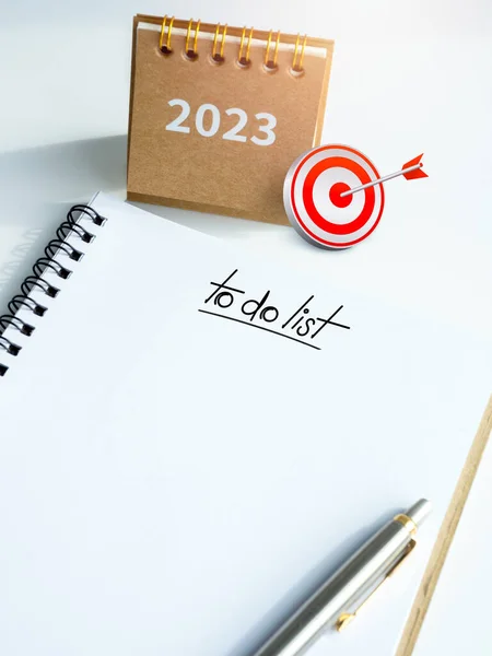3d Target icon on 2023 year desk calendar cover and To do list, text on white blank space on spiral notepad and pen on white background, vertical style. Action plan and goal concept in new year 2023.