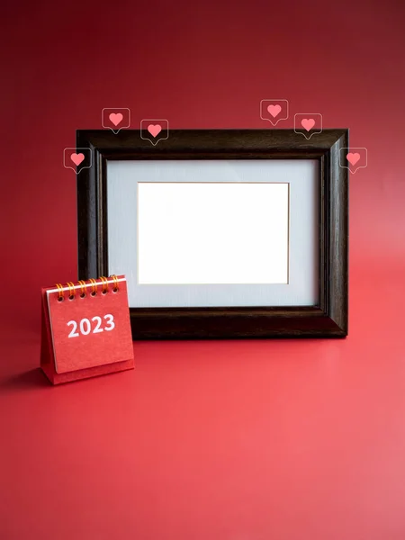 Template for photo frame for card and small 2023 year red desk calendar and love like heart icons on red background, minimalist. Empty white blank space in vintage wooden picture frame, vertical.