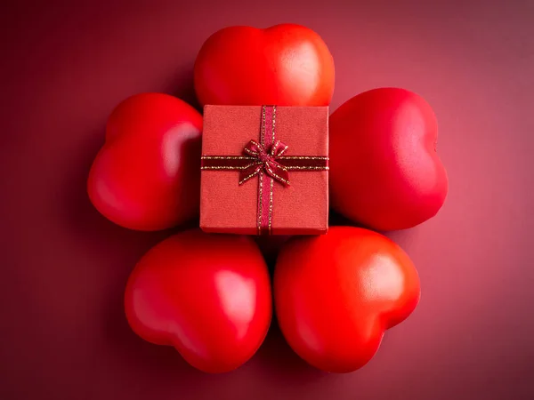 A small red present gift box with ribbon on five heart balls on red background. An essential gift on special days with love, birthdays, New Years, Valentine's Day and anniversaries.